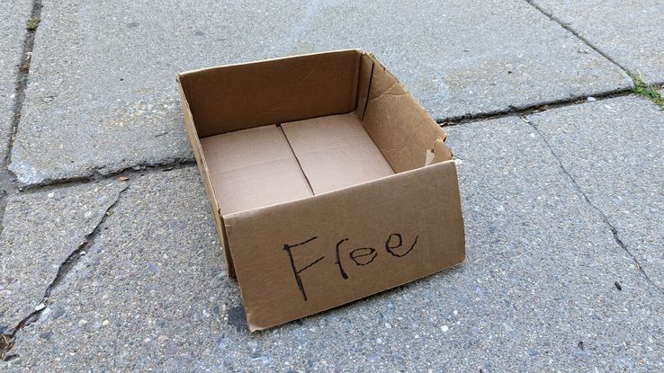 An empty cardboard box on the sidewalk with 'free' hastily written on the side